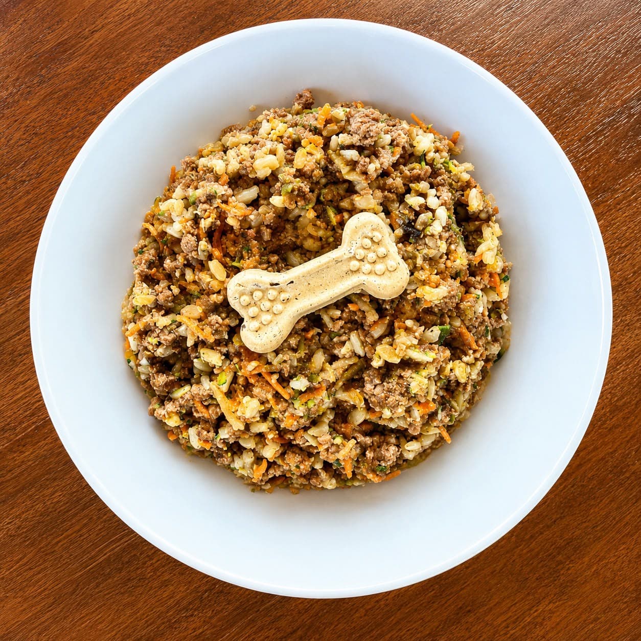 Top-down white bowl of Paw-a-licious food finished with a dog-bone treat, on a wood table